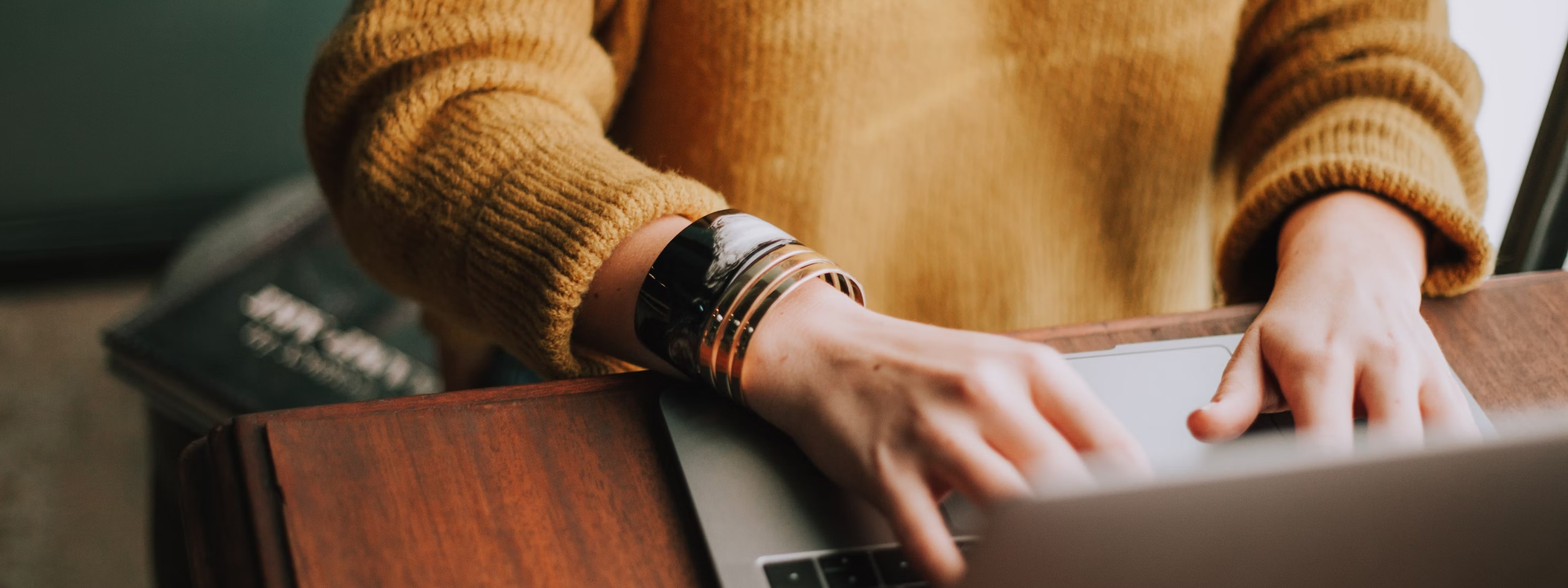 Person in yellow sweater typing on laptop with watch visible