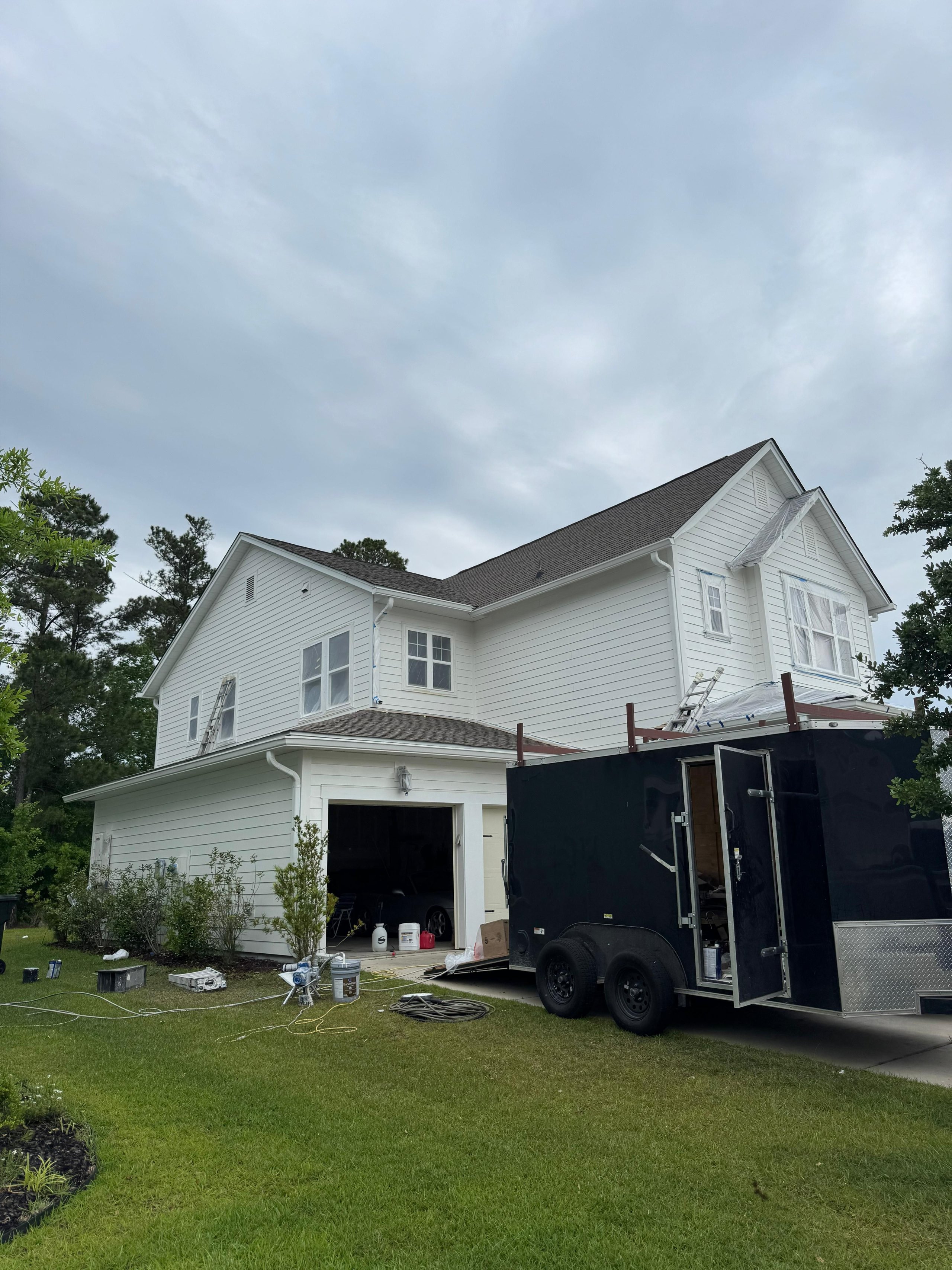 White two-story house with black trailer, painting or renovation equipment