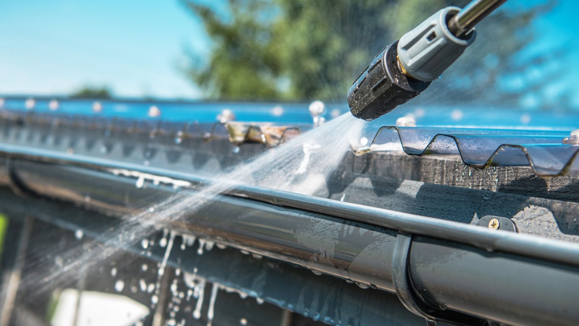 Power washer cleaning gutters with high-pressure water spray