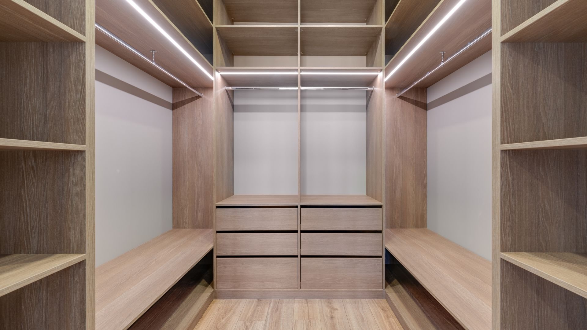 Modern walk-in closet with wooden shelves, drawers, and built-in lighting