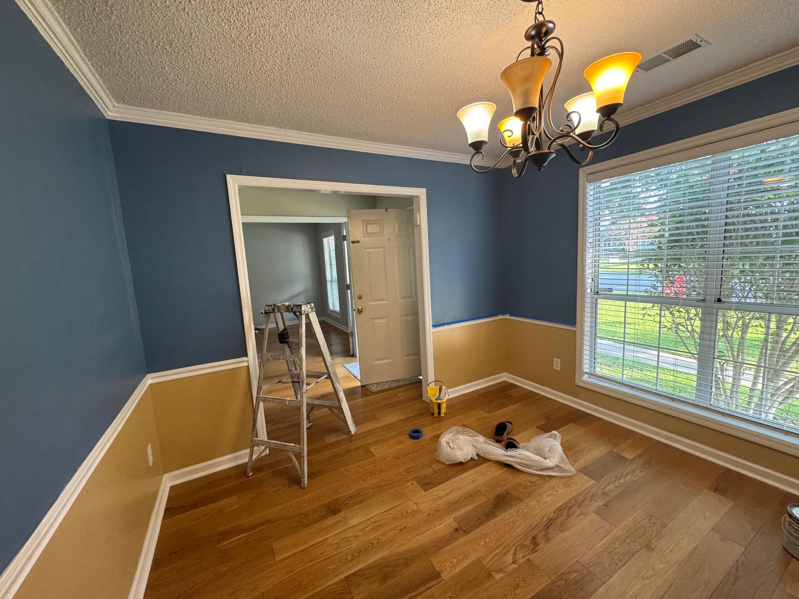 Room mid-painting with blue walls, ladder, and painting supplies