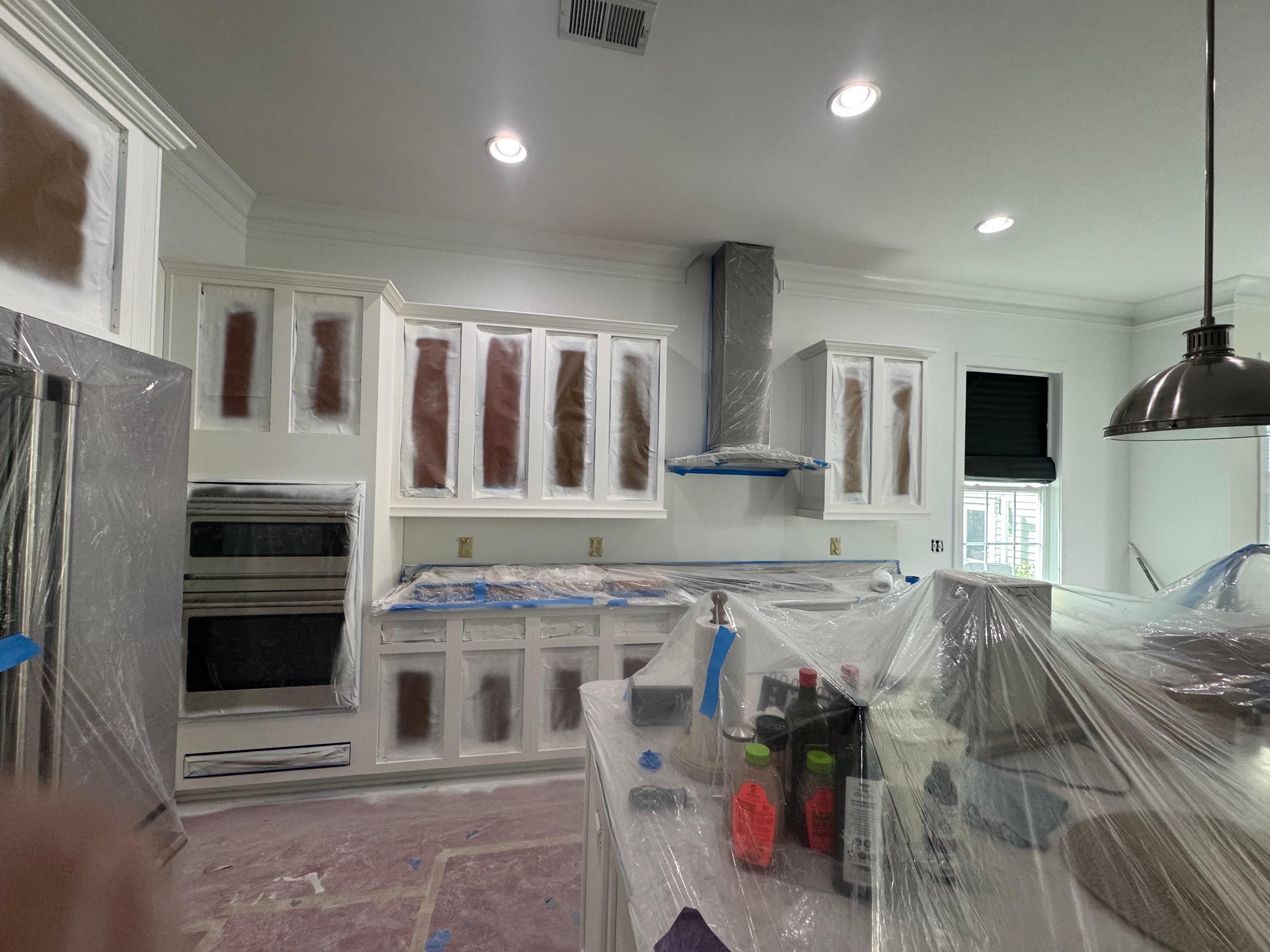 Kitchen renovation in progress with white cabinets and plastic-covered surfaces