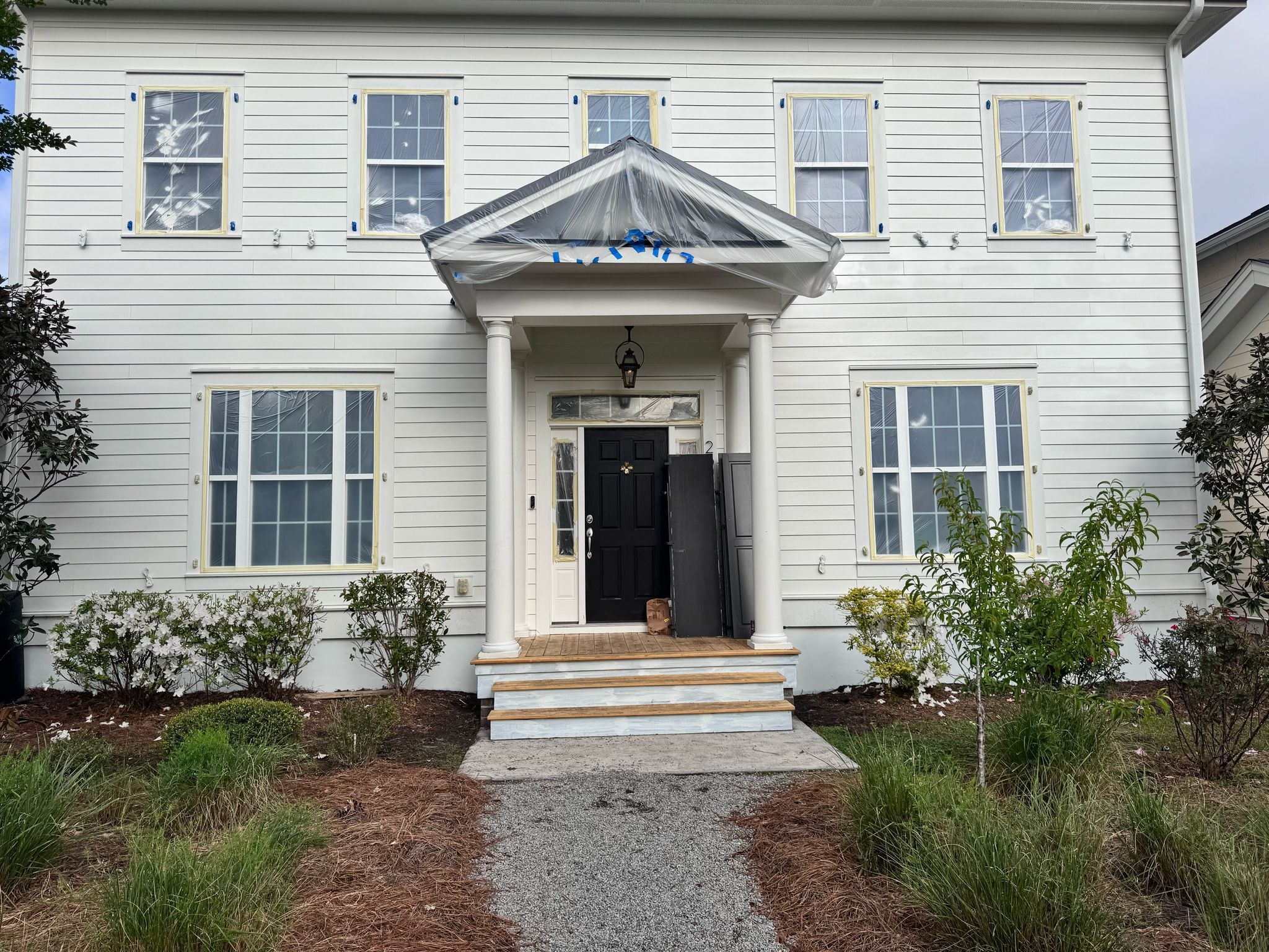 White two-story house with black door, covered front porch, and landscaped yard