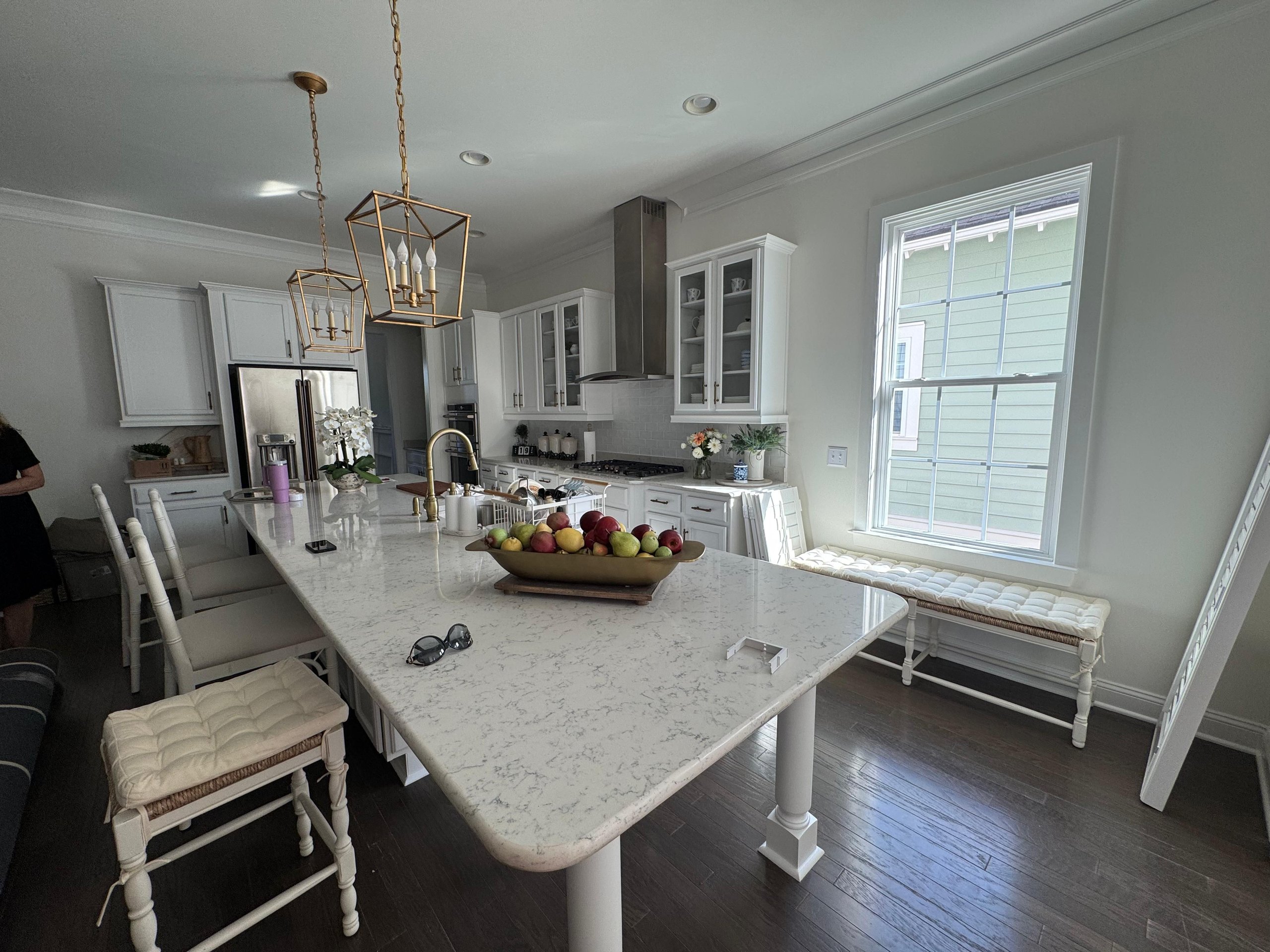 Modern white kitchen with marble island, gold lights, and fruit bowl