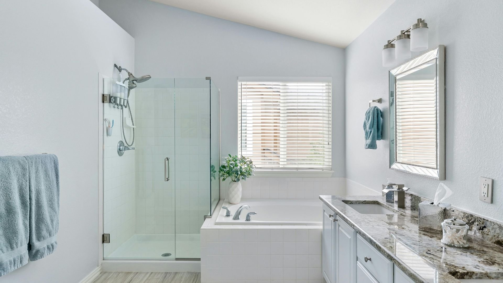Modern white bathroom with glass shower, marble counters, and blue towels