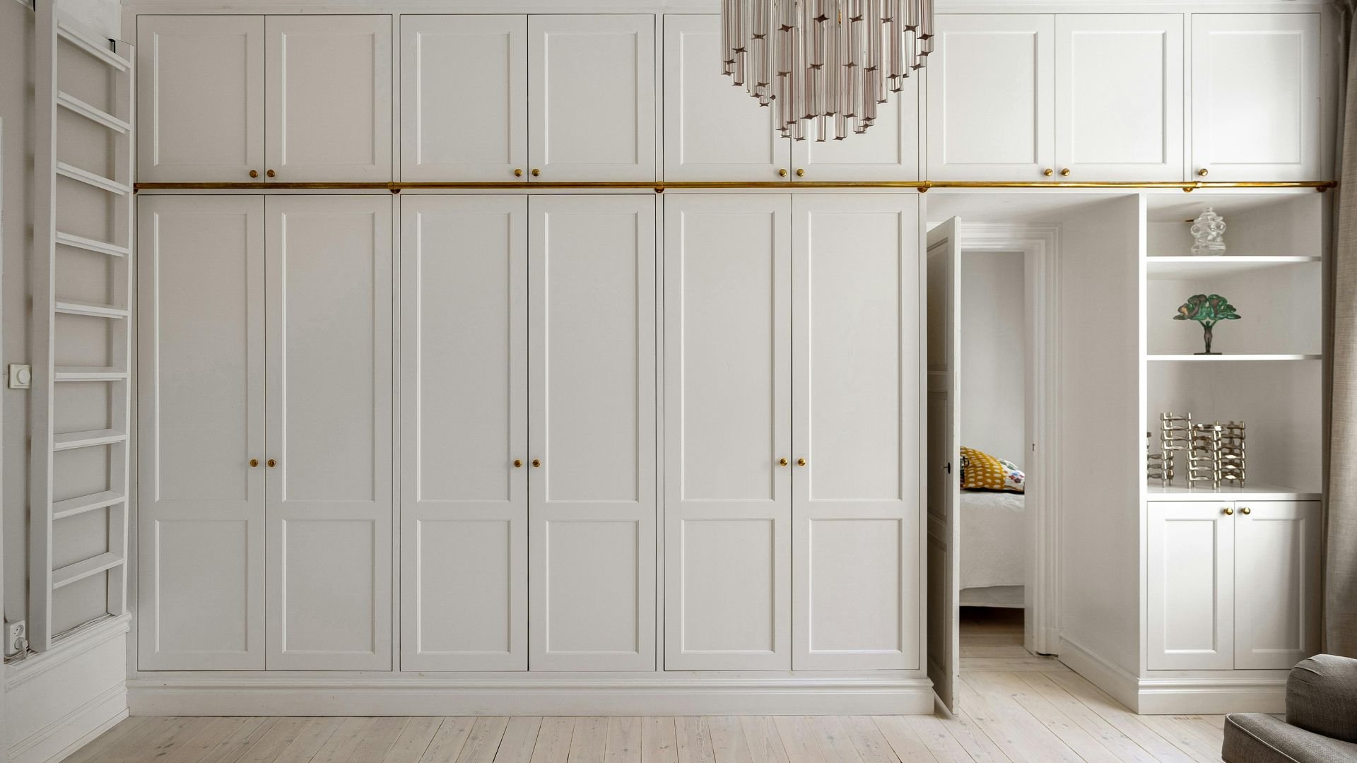 Elegant white built-in wardrobe with golden handles and modern chandelier