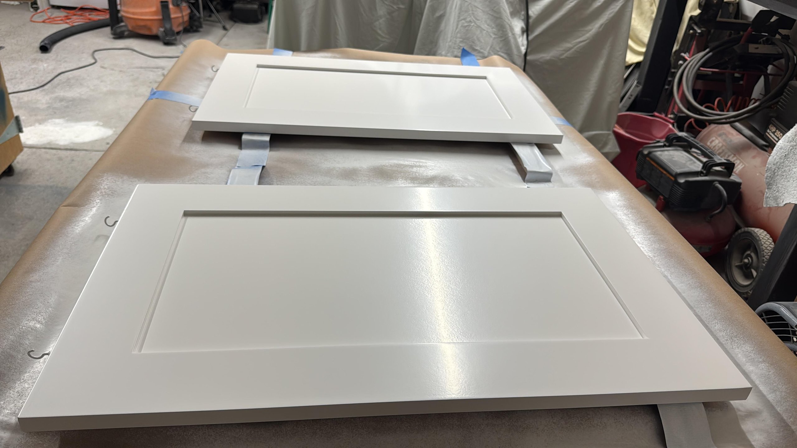 White cabinet doors in workshop, taped and prepared for painting