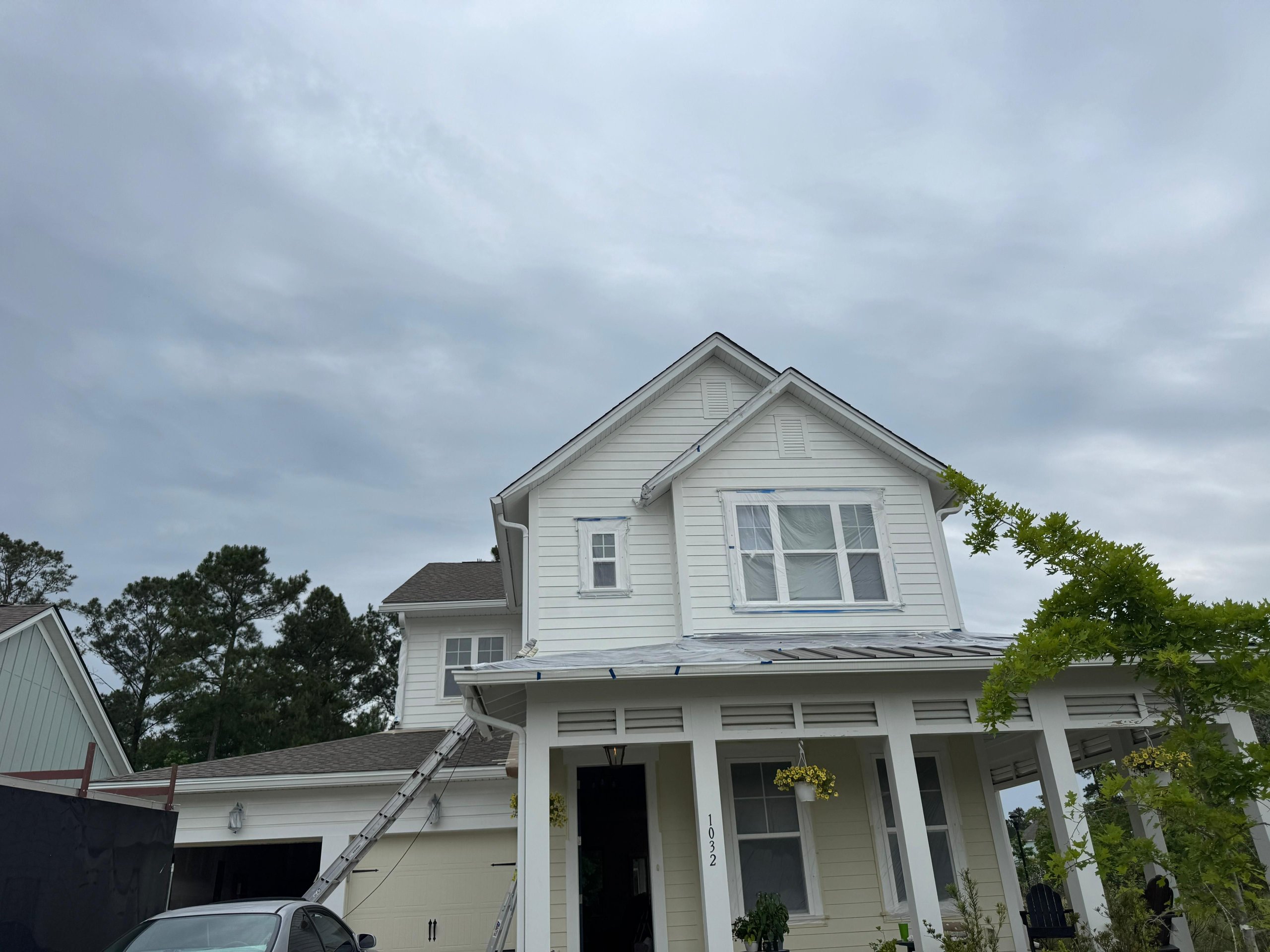 White two-story house with porch under cloudy sky, ladder leaning on roof