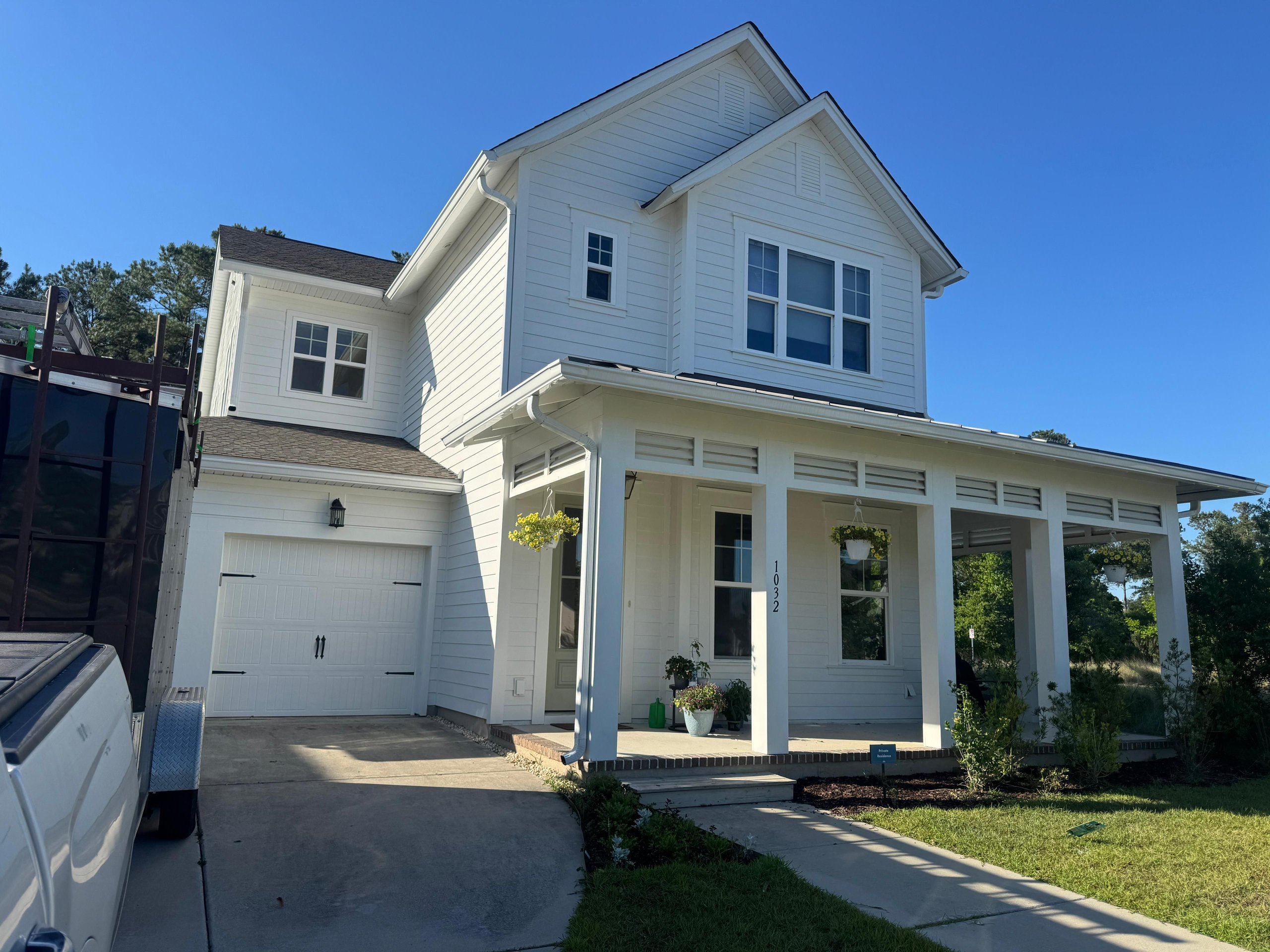 White two-story house with covered porch and hanging plants on sunny day