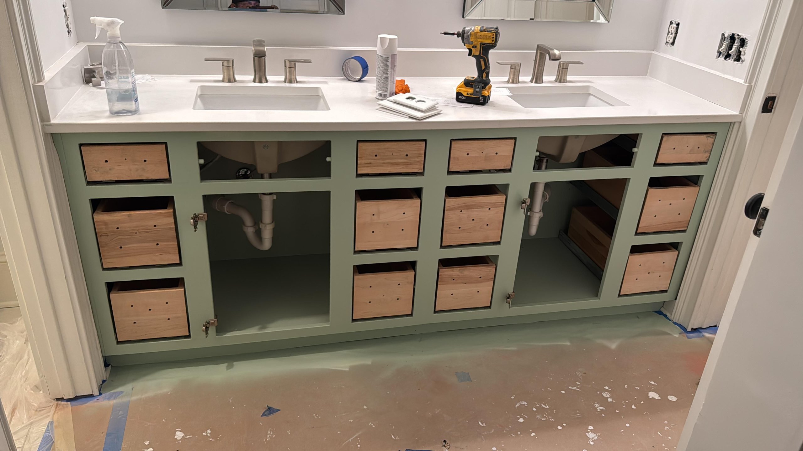 Bathroom vanity in green with wooden drawers, power drill, and cleaning supplies