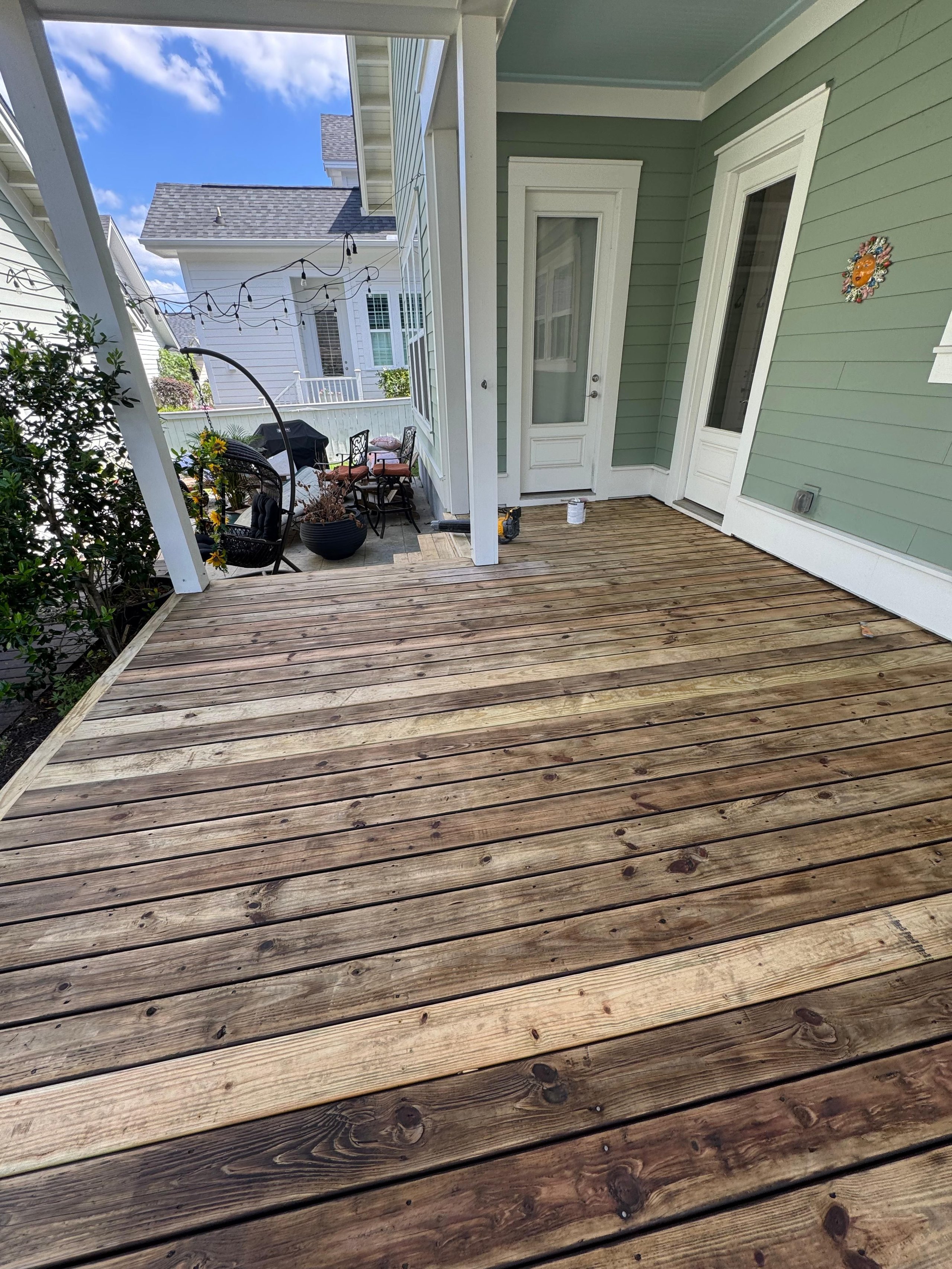Wooden deck with patio furniture and string lights by a green beach house